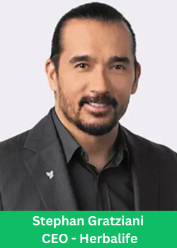A professional headshot of Stephan Gratziani, the CEO of Herbalife, wearing a black suit and smiling confidently.