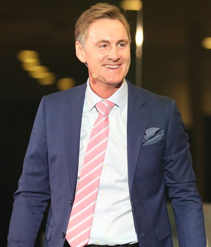 A well-dressed business executive, presumably the CEO of Zinzino, speaking at an event, wearing a navy blue suit with a pink tie.