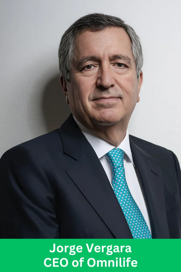 A professional corporate executive profile photo of a man in a suit with a teal tie, standing against a plain background.
