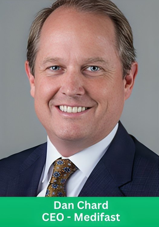 Professional headshot of Dan Chard, the CEO of Medifast, wearing a suit and tie against a grey background.