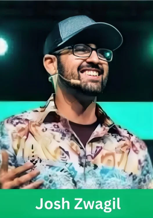 Josh Zwagil smiling on stage wearing a cap and glasses during a business presentation