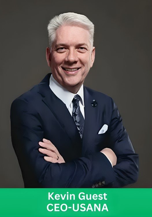 Professional portrait of Kevin Guest, CEO of USANA, wearing a navy blue suit against a dark grey background.