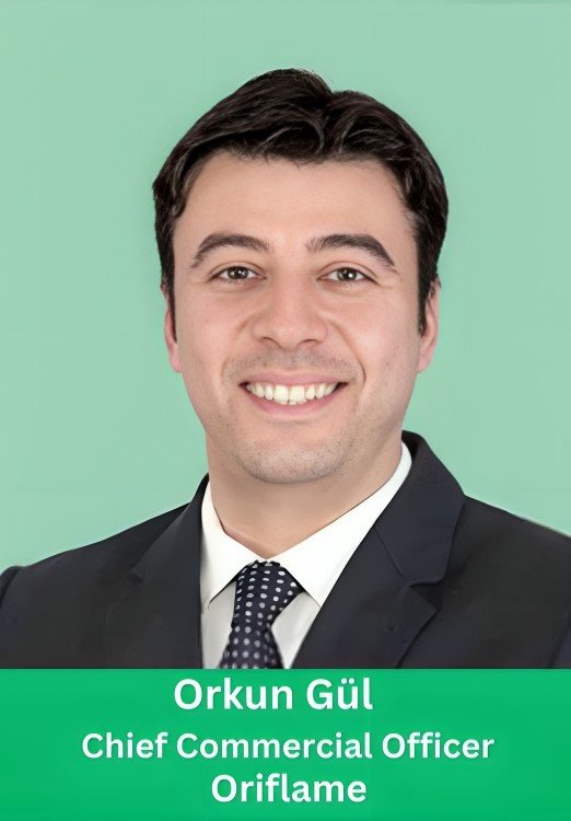 Professional portrait of Orkun Gül, Chief Commercial Officer of Oriflame, smiling in a dark suit and polka dot tie against a light green background.