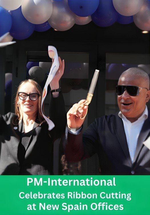 A man and woman with golden scissors are cutting a ceremonial ribbon. The ribbon features the PM-International logo. The background has blue and silver balloons and large glass windows. A green banner with text below states, 'PM-International Celebrates Ribbon Cutting at New Spain Offices'.