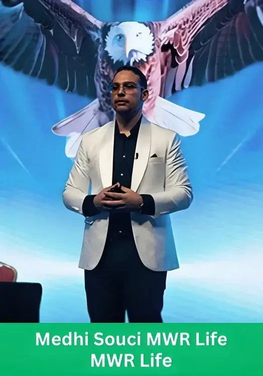 Medhi Souci speaking on stage at an MWR Life event, wearing a white blazer and black shirt, with a large digital graphic of a bald eagle behind him.