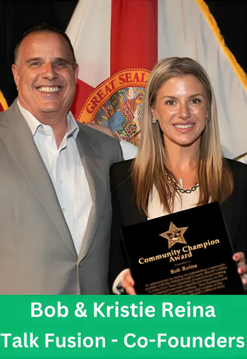Bob and Kristie Reina, Co-Founders of Talk Fusion, smiling while holding a Community Champion Award plaque in front of a flag.
